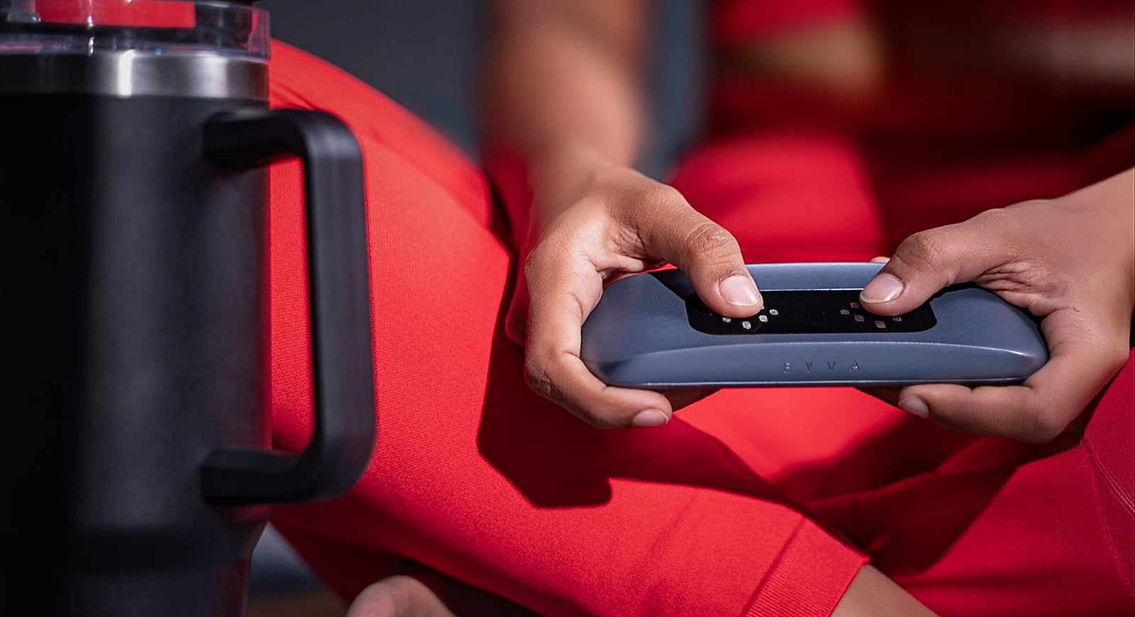 Both thumbs held on EYVA's twin sensor pads, the device resting in two hands beside a water bottle.