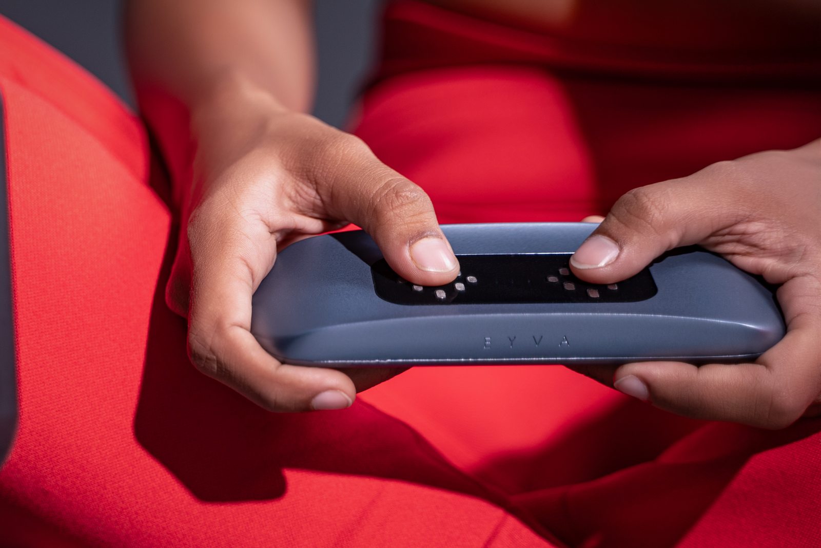 Both thumbs resting on the EYVA sensor pads, the device held in the lap.